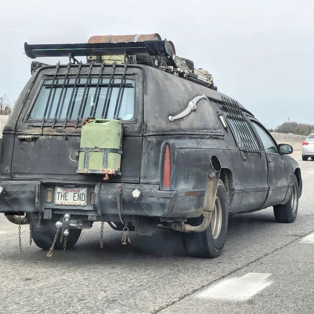 This meme is an image of a heavily modified and armored vehicle, often referred to as a "Mad Max" or "Zombie" car, driving on a road. The vehicle has a large, metal-plated body, a distinctive front grille, and a license plate that reads "THE END". The image is likely intended to be humorous or ironic, perhaps referencing the idea that the vehicle is a last-stand or final-destination vehicle, or that it's a "last-stand" for the driver.
